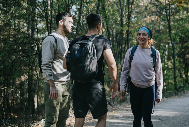Jóvenes amigos exploran montañas boscosas en un día soleado. Ropa deportiva sana y feliz, deportiva, conversan y caminan, disfrutando de la naturaleza y de la compañía de los demás. - Foto, imagen