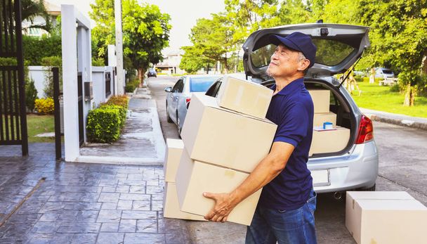 Thuisbezorgbedrijf: Senior mannelijke werknemer staat achterin de truck, registreert de pakketbezorglijst van de klant en kartonnen doos producten op een klembord voor nauwkeurige levering. - Foto, afbeelding