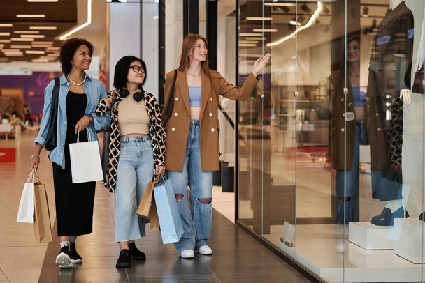 Foto completa de grupo multirracial de chicas jóvenes caminando por el centro comercial observando los escaparates - Foto, imagen