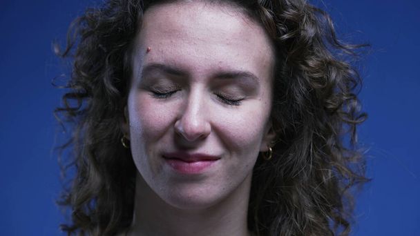 Detailní záběr ženy, jak zavírá oči, s úlevou se usmívá po splnění úkolu. Bez stresu emoce 20s člověk cítí šťastný a uvolněný - Fotografie, Obrázek