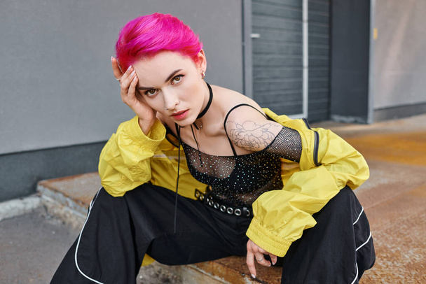 fashionable appealing woman in stylish outfit with pink hair and tattoos looking at camera, fashion - Photo, Image