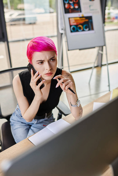 skoncentrowana młoda kobieta z długopisem w ręku rozmawia przez telefon i patrząc na komputer, koncepcja biznesu - Zdjęcie, obraz