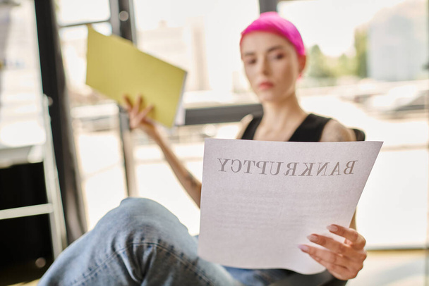 wazig jonge roze harige vrouw in casual kleding lezen document met woord faillissement op het - Foto, afbeelding