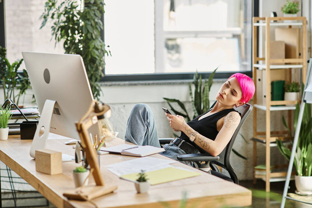 彼女のオフィスで机に座ってコンピュータを見ているカジュアルな衣装のピンクの髪のビジネスマン - 写真・画像