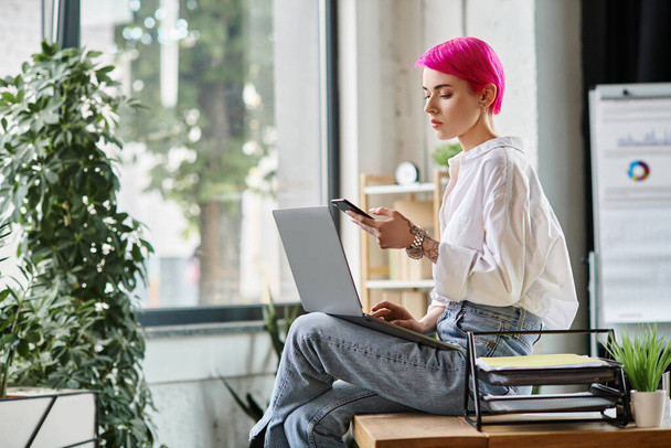 jovem mulher bonita em camisa branca com cabelo rosa olhando para o telefone com laptop em joelhos, negócios - Foto, Imagem