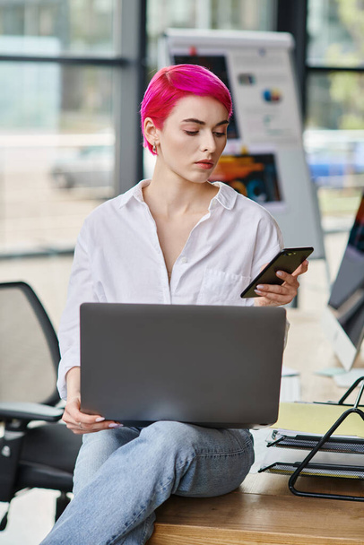 привлекательная молодая женщина-профессионал сидит и смотрит на свой телефон с ноутбуком на коленях, бизнес - Фото, изображение