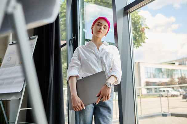 młoda ładna kobieta pracownik w luźnej koszuli i dżinsy trzymając laptopa i patrząc w aparat fotograficzny, biznes - Zdjęcie, obraz