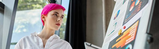 junge attraktive Geschäftsfrau in weißem Hemd mit rosafarbenen Haaren schaut in ihrem Büro auf Schautafeln, Banner - Foto, Bild