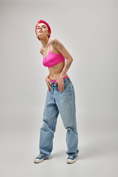 atractiva modelo femenina con tatuajes y cabello rosa inclinándose ligeramente y mirando a la cámara, la moda - Foto, imagen