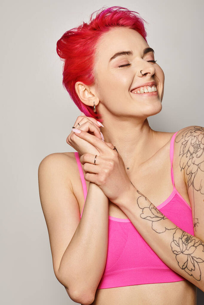 retrato de atraente e satisfeito jovem mulher com cabelo rosa e olhos fechados no fundo cinza - Foto, Imagem