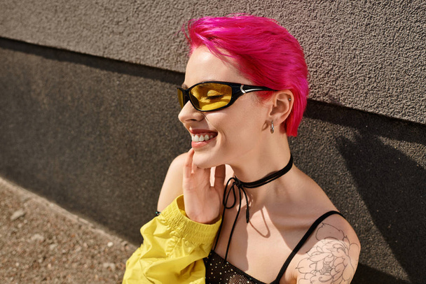 Portret szczęśliwej różowej kobiety w okularach przeciwsłonecznych i modnym stroju pozowanie podczas odwracania wzroku - Zdjęcie, obraz