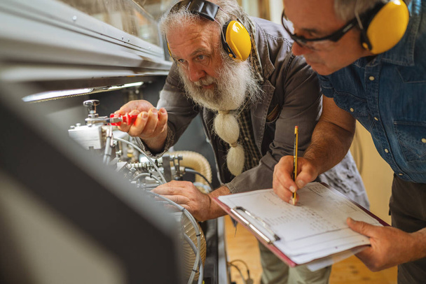 Homens com proteção auricular ajustando máquinas em uma oficina de carpintaria - Foto, Imagem