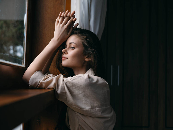 Портрет молодої жінки вдома за вікном з дерев'яною рамою, осіннім настроєм, затишним способом життя, сонною погодою. Високоякісна фотографія - Фото, зображення