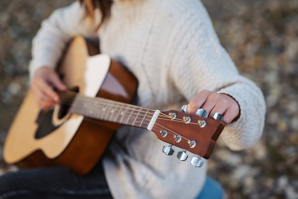 Tyttö virittää akustista kitaraa. Lähikuva käsissä muusikko viritys kitara ulkona syksyllä puistossa - Valokuva, kuva