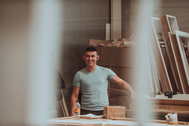 Ein Facharbeiter in der holzbearbeitenden Industrie setzt moderne Maschinen geschickt ein, um Holztüren für den Markt zu bearbeiten und vorzubereiten, was eine nahtlose Mischung aus traditioneller Handwerkskunst und Schneiden darstellt. - Foto, Bild