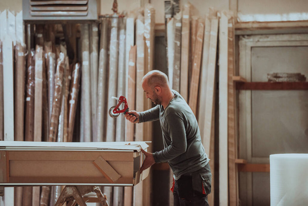 Un trabajador calificado en la industria de la madera es capturado comprometido en el empaquetado meticuloso de puertas, mostrando precisión y atención al detalle como los productos están preparados para las ventas globales y - Foto, Imagen