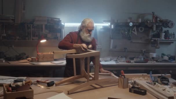 Zoom in shot του πρεσβύτερου Καυκάσου ξυλουργού γυρίζοντας καρέκλα και τρίβοντας τη διαφορετική πλευρά του με γυαλόχαρτο - Πλάνα, βίντεο
