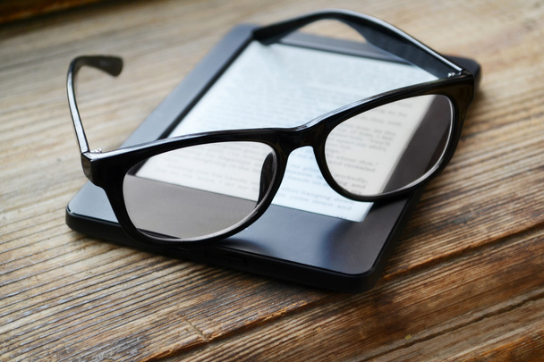 Zwarte ereader met retro bril op houten tafel - Foto, afbeelding