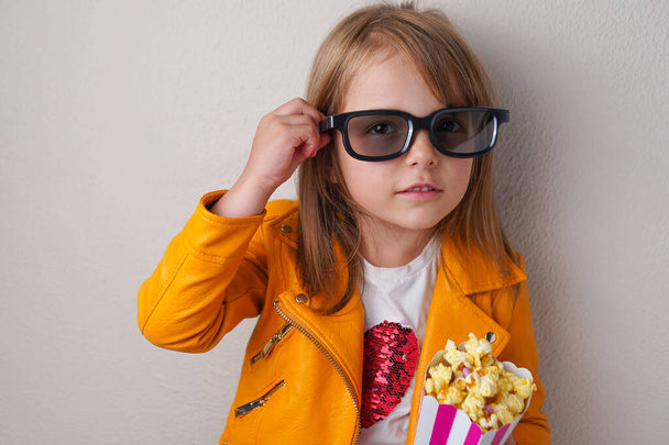 Cute little girl with sweet popcorn and cinema glasses looking directly in the camera - Photo, Image