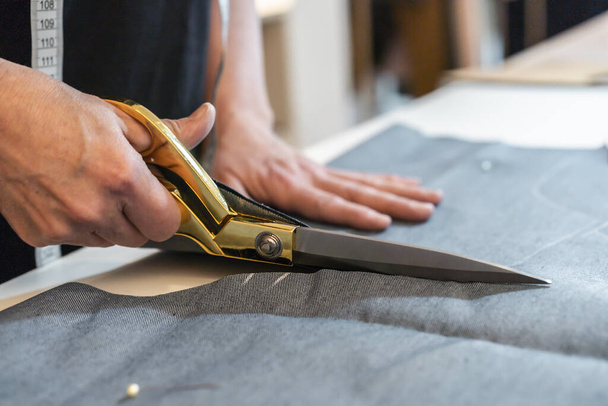 Close-up de mãos designer de moda usando tesoura para cortar têxteis na mesa de trabalho. - Foto, Imagem
