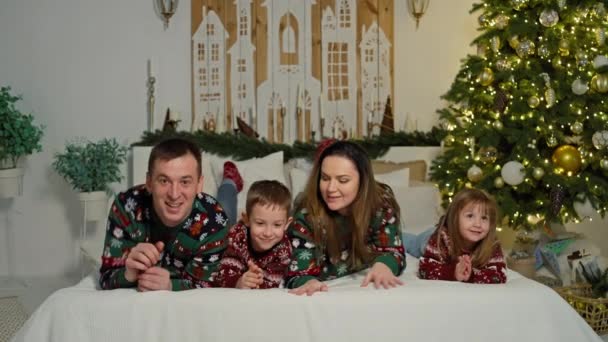 Feestelijke familieportretten: glimlachende moeder, vader, dochter en zoon die vrolijke momenten delen door de kerstboom, magisch kerstgeluk. Hoge kwaliteit 4k beeldmateriaal - Video
