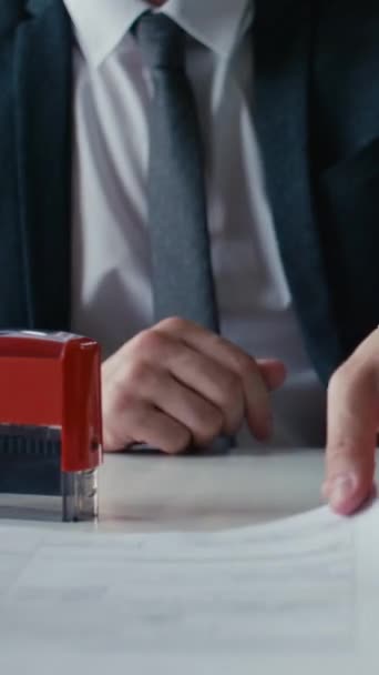 Függőleges vágás lövés egy öltönyös üzletemberről, aki piros pecsétet helyez el a dokumentumokon munkanapokon az irodában. - Felvétel, videó