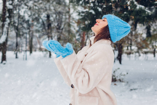 Šťastná žena těší krajinu a zimní počasí pod sněhem procházky v zimním parku na sobě bílý kožich ovčí kůže a teplý pletený modrý klobouk - Fotografie, Obrázek