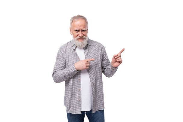 灰色のひげと口ひげを持つ整然とした上級男性は,コピースペースのある白い背景の平らなシャツとジーンズを着ています. - 写真・画像