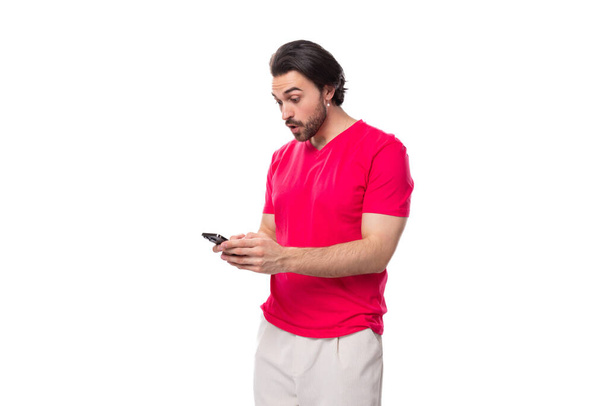 赤いTシャツを着た黒い髪の若いハンサムな男が電話でメッセージを書く. - 写真・画像