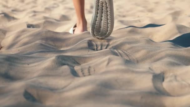 Közelkép a fiatal nő lábáról, amint fehér papucsban vagy papucsban sétál a forró napon, fehér homokon. Kamera követi a nőt, mozgás. - Felvétel, videó
