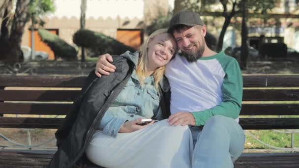 Portrait of two young partners, couple in romantic relationship, Caucasian family flirting, sitting on bench, handsome guy kissing beautiful blonde woman hugging outdoors, High quality 4k footage - Footage, Video