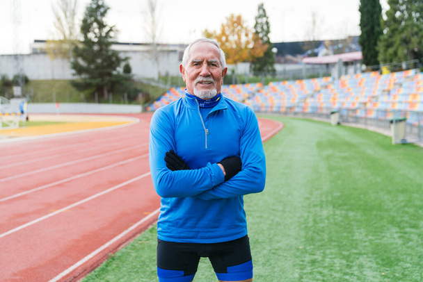 In forma anziano atleta di sesso maschile con le braccia incrociate sorridente fiducioso alla pista dello stadio. - Foto, immagini