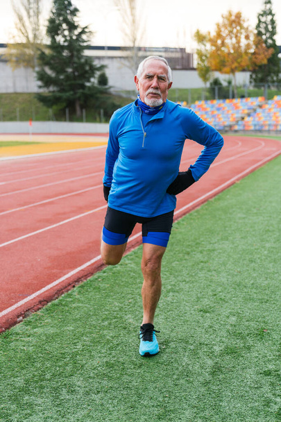 Mature athlète caucasien en bleu prend une pause sur la piste de course, incarnant un mode de vie senior actif - Photo, image