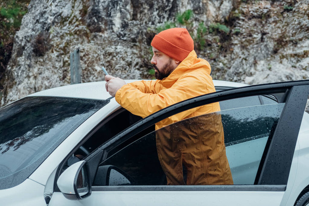 Homme prend une vidéo verticale sur un téléphone portable de la voiture sur la route en automne belle forêt - Photo, image