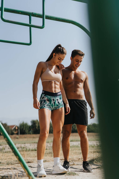 Motivated couple doing pull ups on metal bars in park. Enjoying sunny day, embracing healthy lifestyle and fitness routine. Inspiring others with dedication and sportsmanship. - Фото, изображение