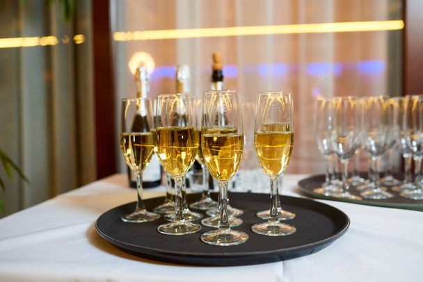 Detailní fotografie sklenic naplněných šampaňským na černém podnose na bílém stole. Nový rok, firemní oslavy v práci, svatba, narozeniny nebo vánoční večírek. - Fotografie, Obrázek