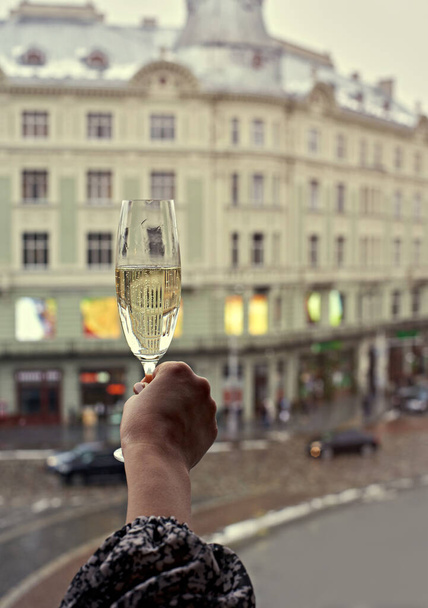 La maison d'en face se reflète dans une coupe de champagne tenue par une femme par la fenêtre dans un appartement dans le centre-ville.Vacances, Nouvel An, Noël. Journée des filles. Main féminine avec une coupe de champagne - Photo, image