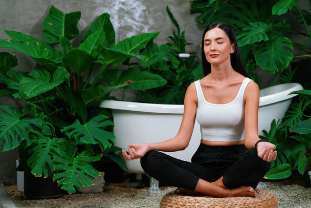 Młoda kobieta uprawia poranną jogę i medytację w naturalnym ogrodzie z liściem roślin, ciesząc się samotnością i praktykując pozy medytacyjne. Aktywność uważności i zdrowy tryb życia umysłu. Blithe - Zdjęcie, obraz