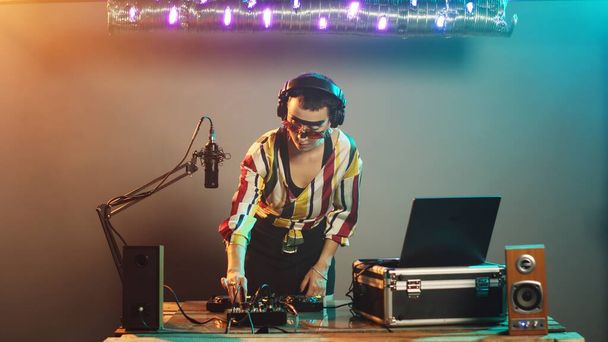DJ μουσικός που χρησιμοποιεί πικάπ για να αναμίξει techno ήχους, παράγοντας μουσική σε επαγγελματικό μίξερ με ηλεκτρονικά κουμπιά μπάσο. Γυναίκα καλλιτέχνης κάνει remix στερεοφωνική παράσταση στο κλαμπ. Σφηνάκι τρίποδα. - Φωτογραφία, εικόνα