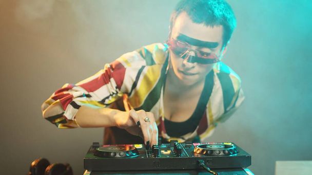 Young cool artist working as dj with turntables, mixing modern remix with bass and audio stereo equipment. DJ performer playing music with mixer and disc buttons. Handheld shot. - Photo, Image