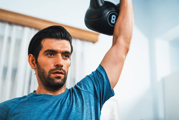 Corpo atlético e ativo desportivo homem levantando kettlebell peso para o ganho muscular alvo eficaz em casa alegre como conceito de corpo saudável ajuste estilo de vida de treino em casa. - Foto, Imagem