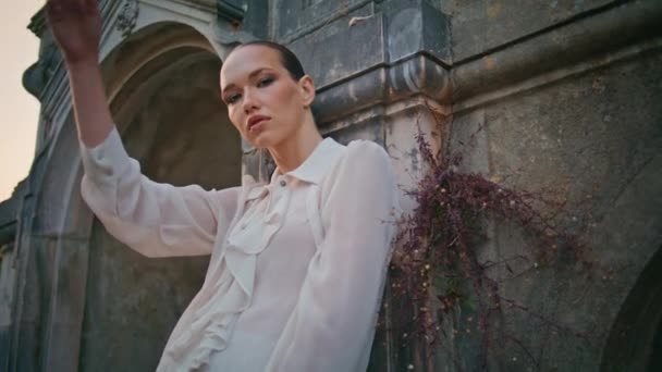 Beautiful girl posturing at medieval castle summer evening close up. Luxurious woman looking camera confidently leaning on old stone wall. Attractive glamorous model standing outside ancient building. - Footage, Video