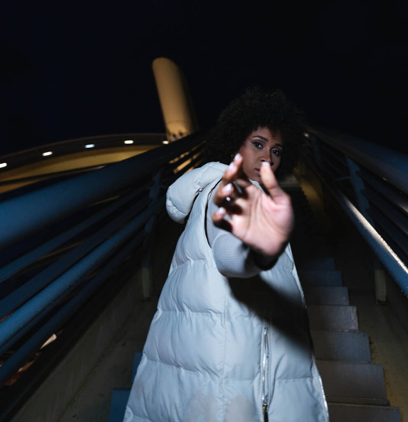 donna afroamericana guardando la fotocamera in un ambiente urbano di notte - Foto, immagini