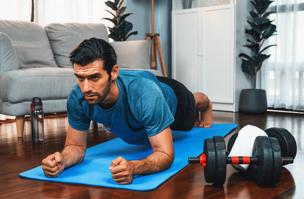Atlétikai és sportos férfi csinál deszka fitnesz szőnyeg alatt otthoni testedzés edzés gyakorlása ülésén a fitt fizikum és az egészséges sport életmód otthon. Vidám otthoni edzés edzés képzés. - Fotó, kép