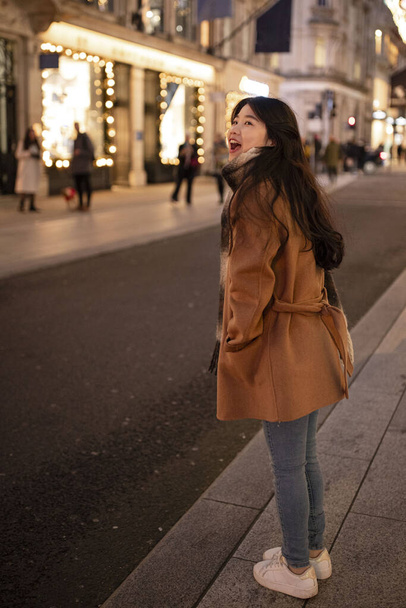 Güzel Asyalı kadın, yoğun şehir caddesinde akşam vakti taksi çağırıyor..  - Fotoğraf, Görsel