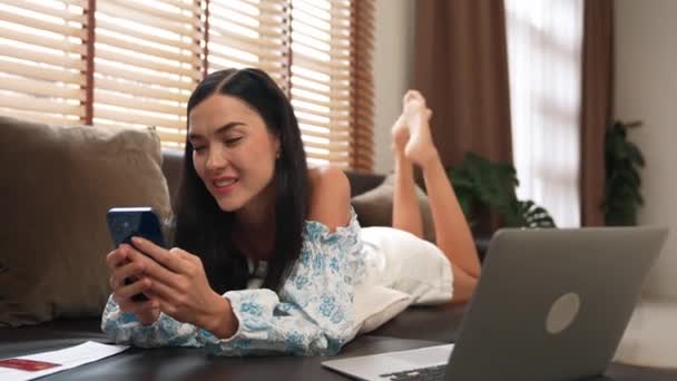 Kanepede yatan genç bir kadın internet bankacılığı için kredi kartıyla dizüstü bilgisayar kullanıyor. Evdeki online ödeme kapısından alışveriş yapıyor. Modern ve uygun online satın alma. Blithe - Video, Çekim