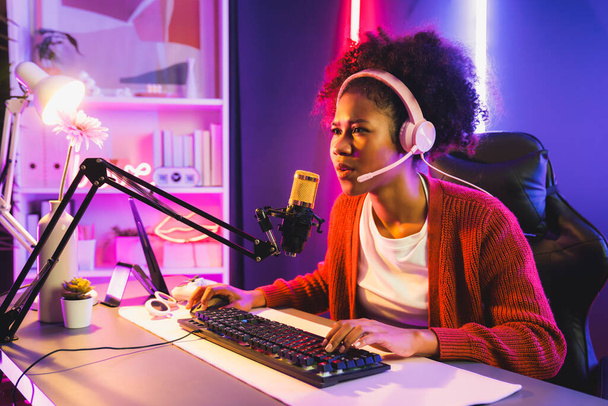 Africká americká dívka streamer hrát online boj s Esport zkušený tým nosí sluchátka v neonové barvě osvětlovací místnosti. Mluvit s ostatními hráči plánování strategie vyhrát konkurenty. Tastemaker. - Fotografie, Obrázek
