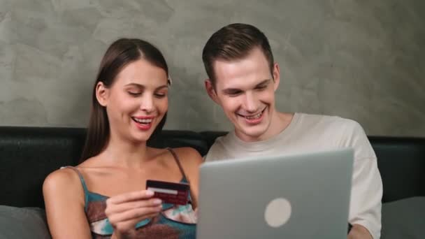 Genç çift, kredi kartıyla ödeme yapmak için internet üzerinden ödeme uygulaması ve dijital cüzdan kullanarak yatak odasında oturuyor. Mobil internet üzerinden alışveriş ve modern alımlar. Düzenle - Video, Çekim