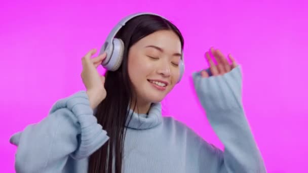 Musik, Tanz und Kopfhörer mit einer asiatischen Frau im Studio isoliert auf rosa Hintergrund zum Streamen von Audio. Lächeln, Freiheit und Energie mit einer glücklichen jungen Frau beim Hören einer Radio-Playlist. - Filmmaterial, Video