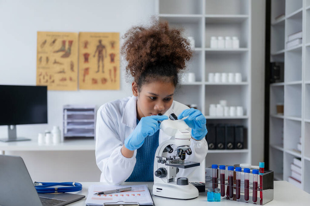 Afrikai női orvos kutatja sclerosis segítségével mikroszkóp egy kórházi laboratóriumban. - Fotó, kép